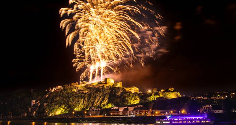 Feux d'artifice au-dessus d'une rivière et d'une forteresse la nuit.