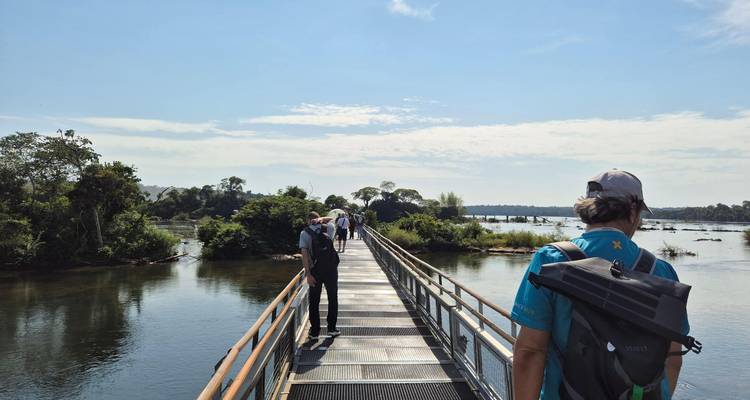 Visitors walk a metal boardwalk over water toward the edge of Iguazu Falls.