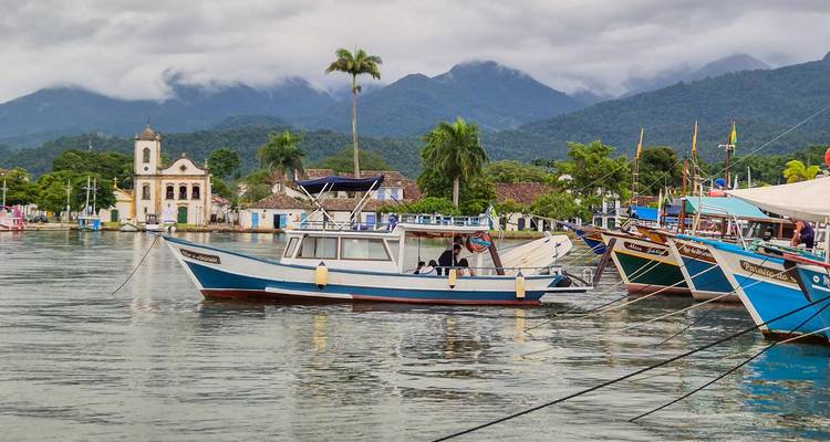 Colourful fishing boats float in Paraty’s colonial harbour backed by misty mountains.