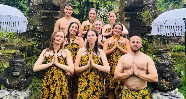 Los turistas visten sarongs tradicionales y posan con las palmas juntas frente a las estatuas del templo balinés.