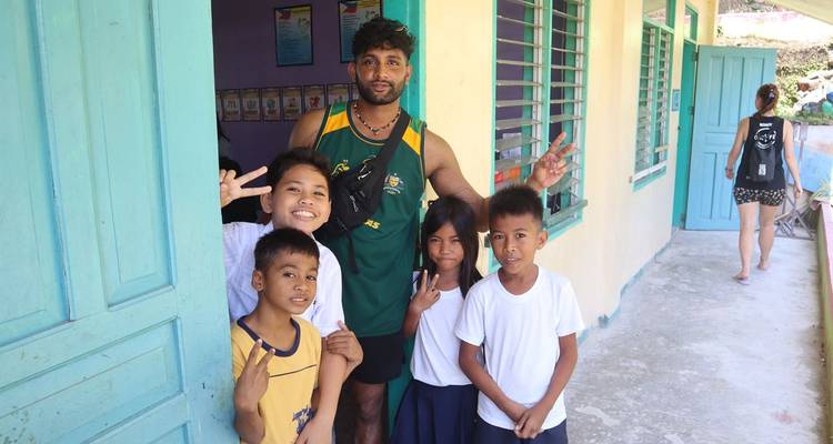 Un voyageur posant avec des écoliers souriants devant une salle de classe de village aux couleurs éclatantes.