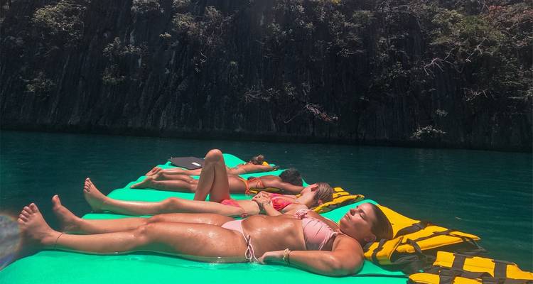 Les voyageurs prenant un bain de soleil sur un matelas flottant dans une eau émeraude sous des parois de calcaire sombre.