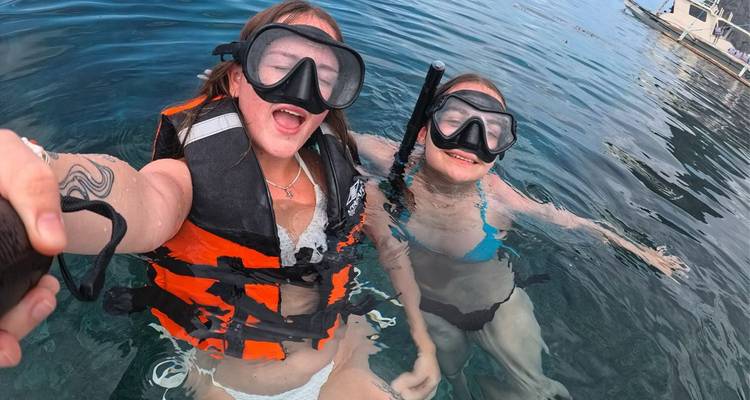 Selfie de deux plongeurs en apnée riant dans une eau bleue cristalline, portant des masques et des gilets de sauvetage.