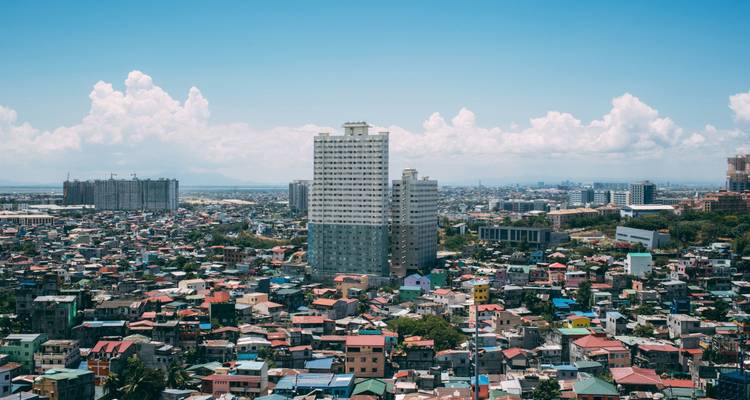 Skyline de Manille en journée avec une tour de grande hauteur au-dessus de denses logements urbains sous un ciel bleu.