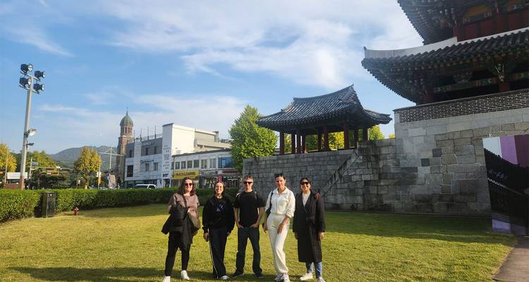 Small group of travellers smile for a photo on the lawn beneath a traditional Korean city gate.