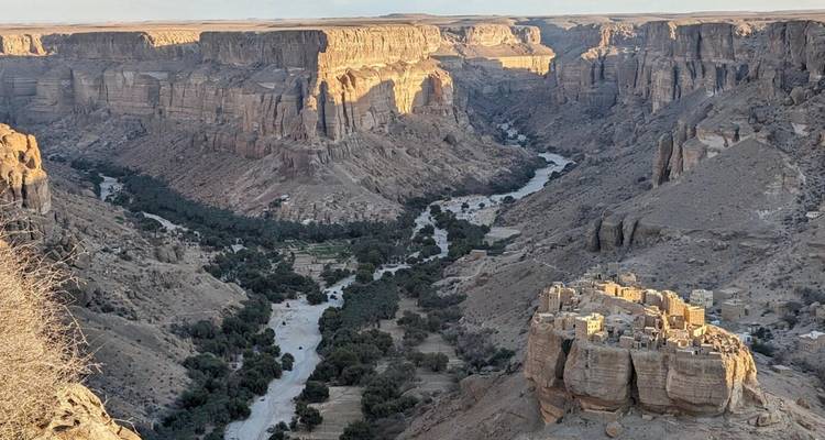 Paisaje del Gran Cañón con un oasis fluvial y un pueblo en la cima de una colina bañado en suave luz vespertina.