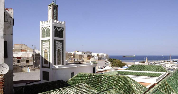 Minarete y tejados con un puerto marítimo al fondo.