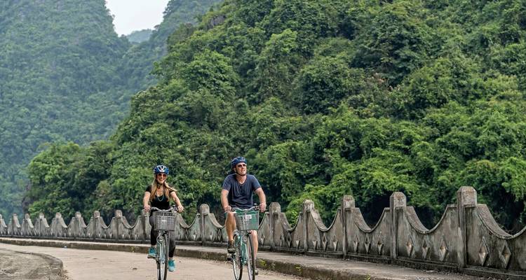 Zwei Menschen fahren Fahrrad auf einem malerischen Weg mit üppigem Grün im Hintergrund.