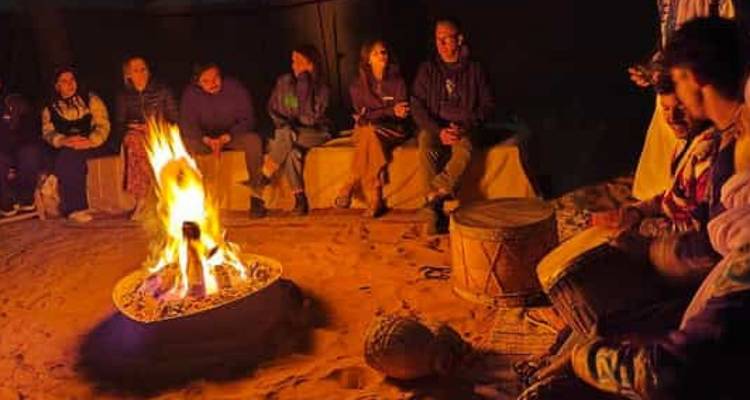 Group of people sitting around a campfire in an outdoor setting.
