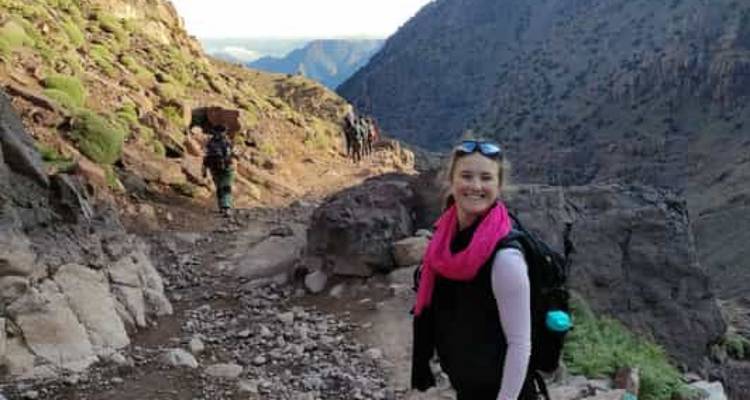 A person on a mountainous hiking trail with distant peaks.