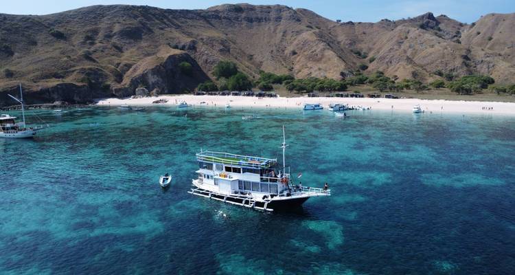 Vue de drone d'un petit bateau-logement blanc ancré dans une eau turquoise cristalline près d'une plage de sable de Komodo.