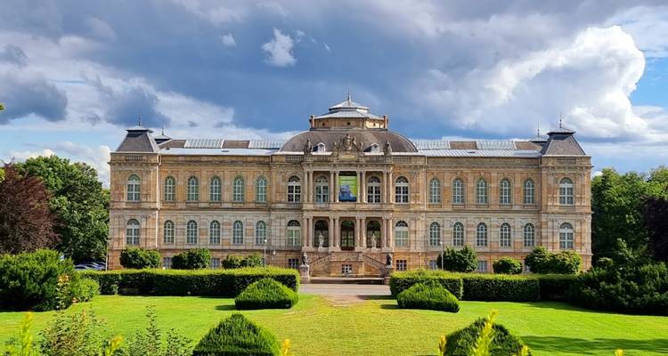 Un grand bâtiment historique avec une architecture ornée et un jardin bien entretenu devant.