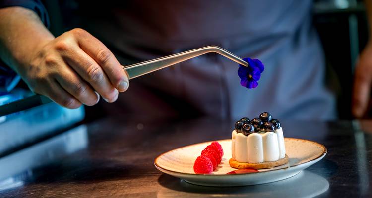 Chefs hand die een bloem op een gourmet dessertbord plaatst.