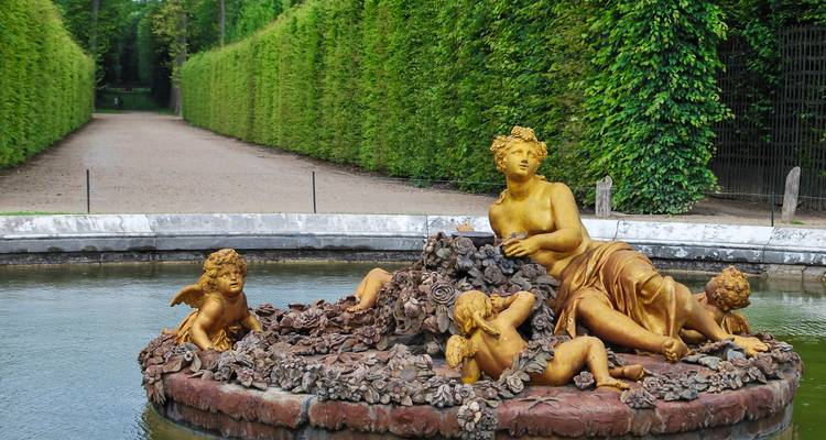 Gouden fonteinbeelden in een netjes gesnoeide tuin.