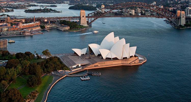Aerial view of Sydney Opera House on Bennelong Point with Harbour Bridge and blue harbour waters.