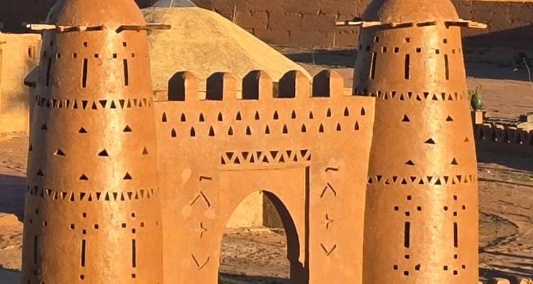 Estructura de arcilla con torres y recortes decorativos en un entorno desértico.