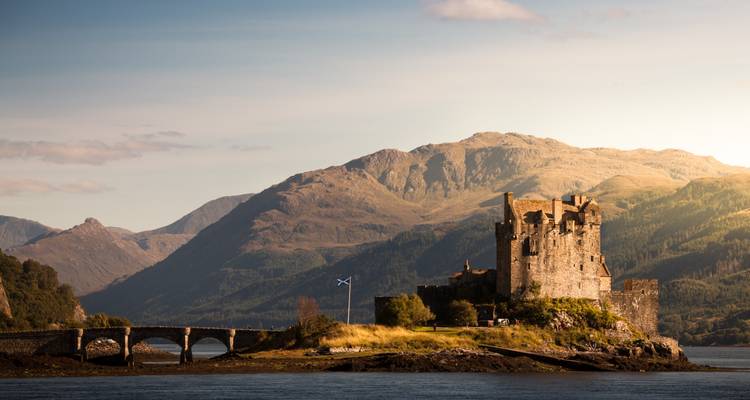 Historic castle with mountains in the background and a Scottish flag.