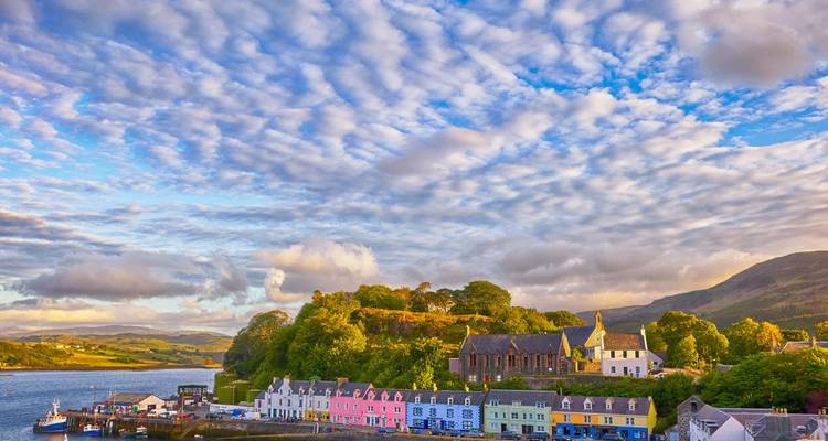 Village portuaire coloré de Portree avec des maisons aux teintes pastel sous un ciel dramatique strié de nuages.
