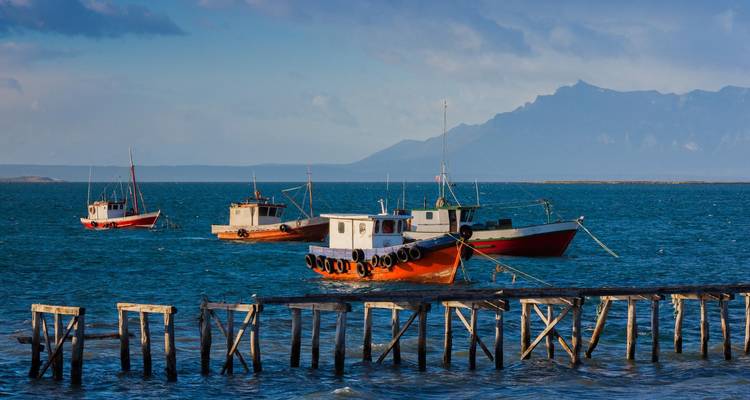 Vissersboten afgemeerd bij een houten pier met bergen op de achtergrond.