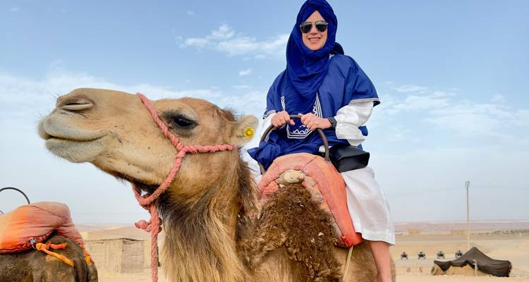 Eine Person, die auf einem Kamel in einer Wüstenlandschaft reitet.