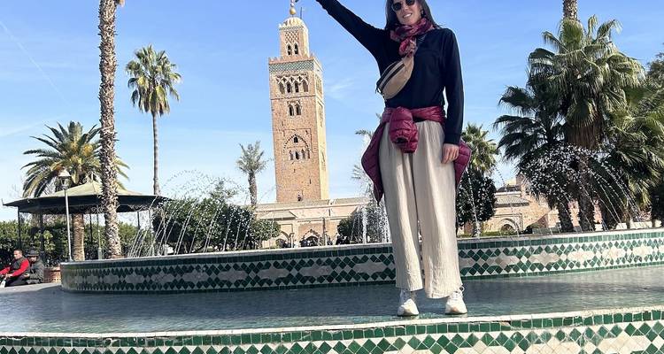 Personne posant devant un grand minaret dans une place ensoleillée.