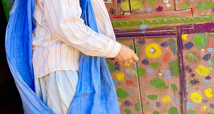 Vue rapprochée d'une personne en robe traditionnelle ouvrant une porte en bois peinte de couleurs vives au Maroc.