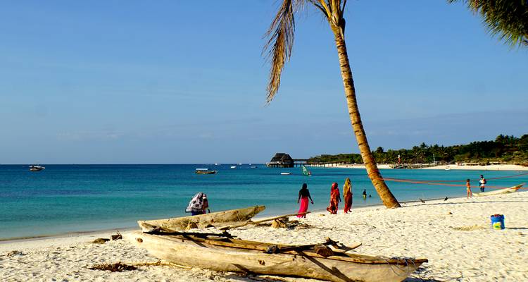 A tropical beach with palm trees, local people, and boats in the water.
