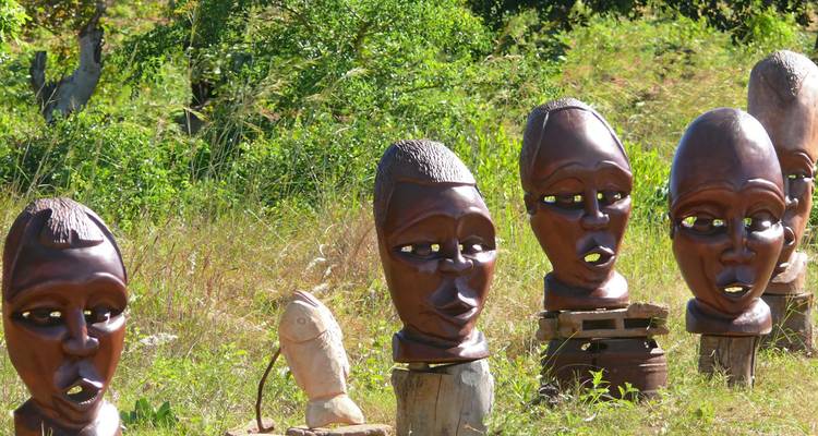 Met de hand gesneden houten Afrikaanse maskers tentoongesteld in een outdoor ambachtskraam omgeven door groen.