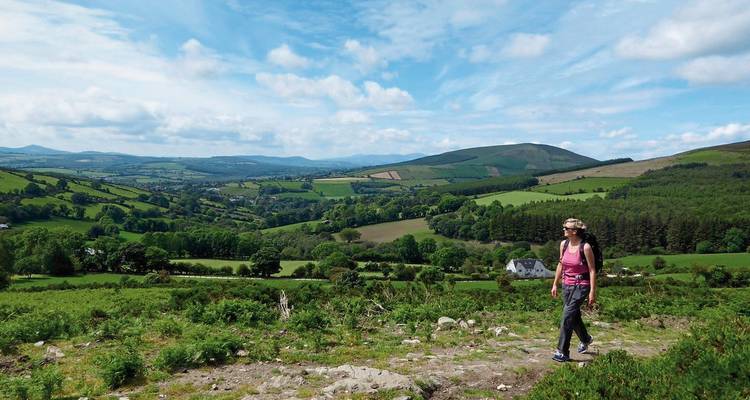 Person walking along a trail with panoramic countryside views.