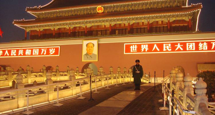 Nighttime view of Tiananmen Square with a large portrait and signage.