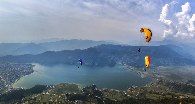 Des parapentistes volant au-dessus d'un grand lac avec des montagnes en arrière-plan.