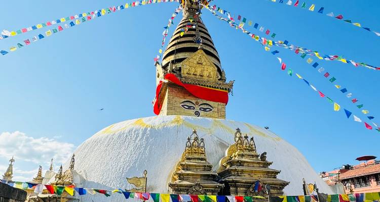 Stupa bouddhiste avec drapeaux de prière sous un ciel bleu clair.