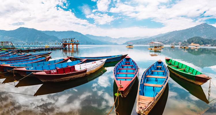Bateaux colorés sur un lac réfléchissant avec des montagnes en arrière-plan.