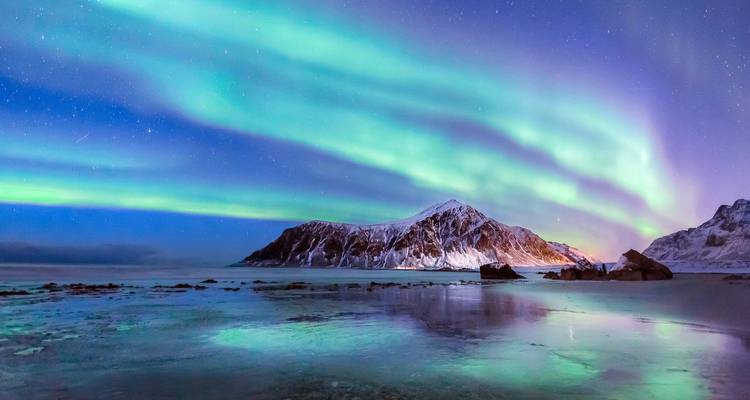 Aurora boreal sobre montañas nevadas y agua reflectante.