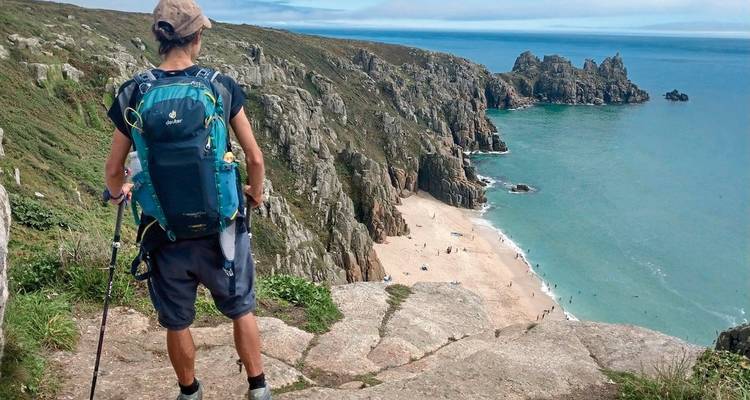 Hiker overlooking a cliffside and beach with turquoise waters.