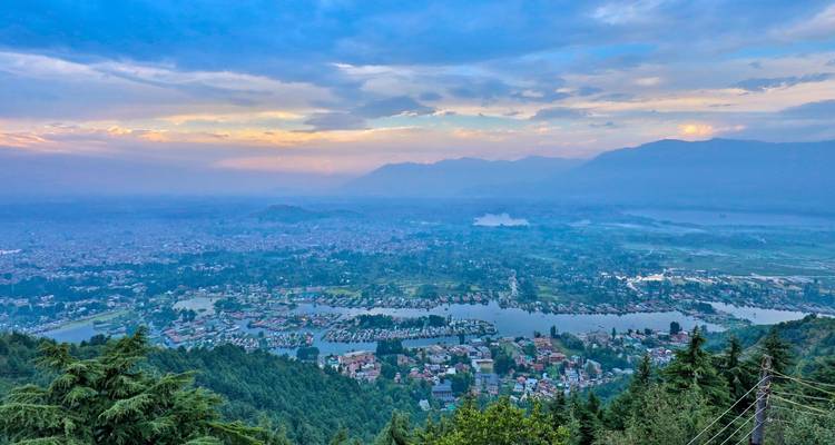 Panoramic view of a city alongside river with mountains in the background.
