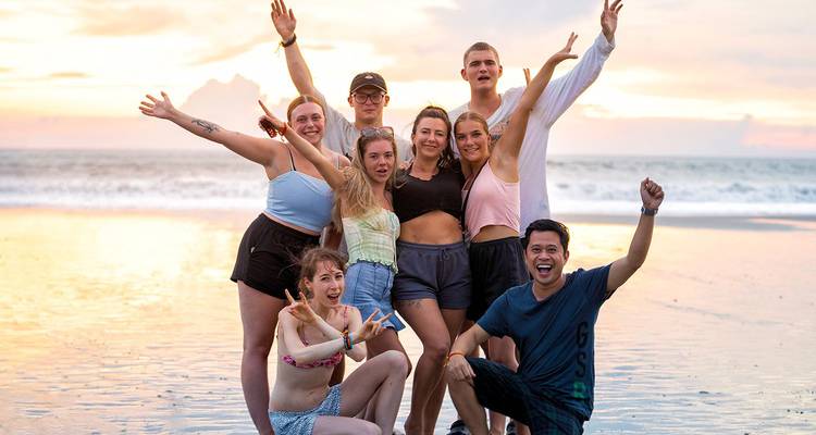 Vrolijke groep jonge reizigers die poseren op een zandstrand bij een kleurige zonsondergang