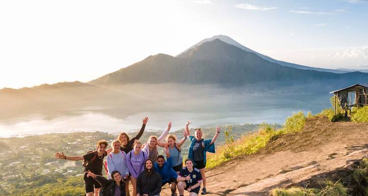 Blije wandelaars die vieren op een vulkanische top met uitzicht op het Batur-meer bij zonsopgang