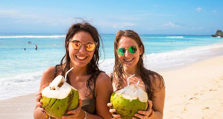 Lachende vrouwen in zwempakken die verse kokosnoten vasthouden op een helder witzandstrand