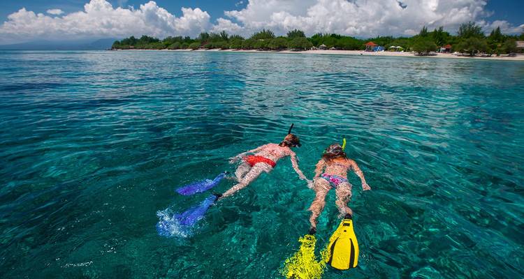 Twee snorkelers met kleurrijke vinnen die kristalhelder tropisch water verkennen dicht bij een zandstrand