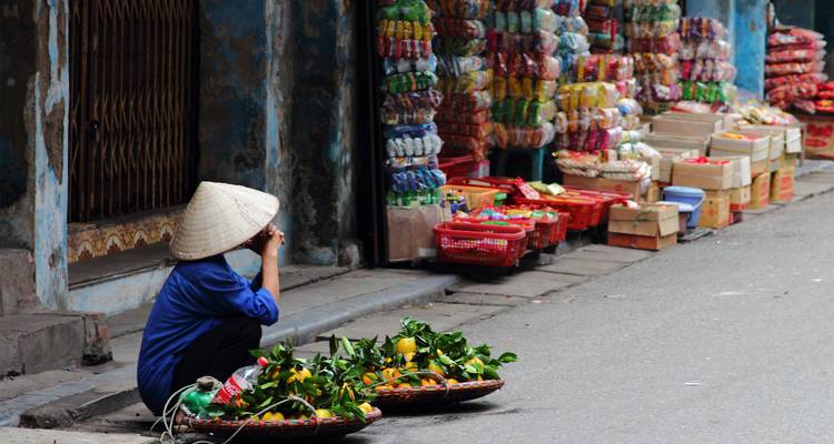 Een lokale verkoper die naast zijn fruitmanden op straat zit.
