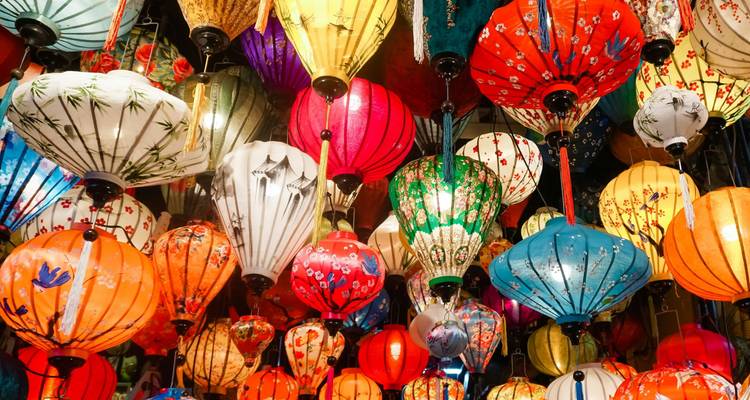 Una cascada de coloridos faroles de seda cuelga densamente sobre tu cabeza en un puesto del mercado de Hoi An.