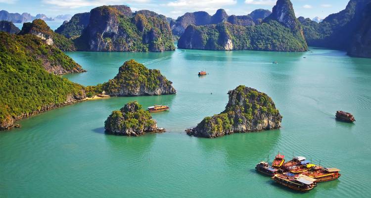 Vista aérea dramática de la bahía de Halong de color esmeralda salpicada de islotes de piedra caliza cubiertos de selva y barcos de crucero.