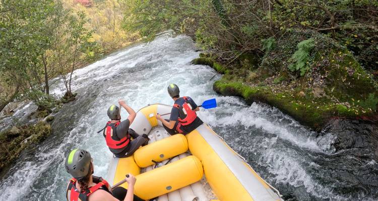 Vue depuis l'arrière d'un radeau gonflable jaune alors que trois pagayeurs casqués naviguent dans les rapides d'une rivière forestière aux eaux tumultueuses.