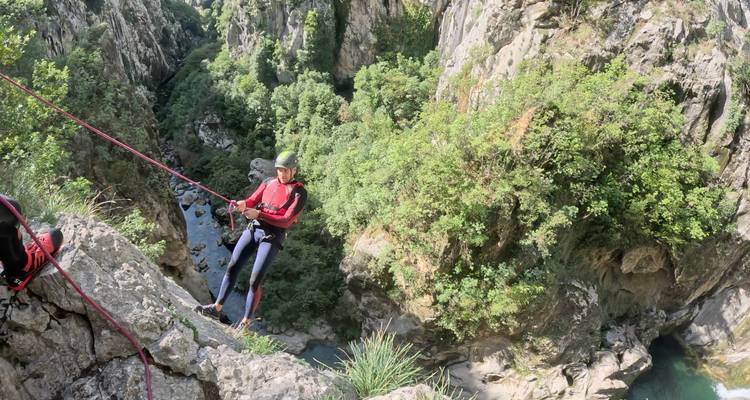 Descente en rappel le long d'une paroi rocheuse de canyon sécurisée par une corde rouge au-dessus d'une rivière étroite bien en dessous.