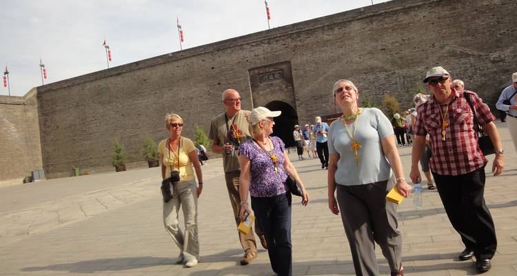 Toeristen die langs een historische stadsmuur wandelen.
