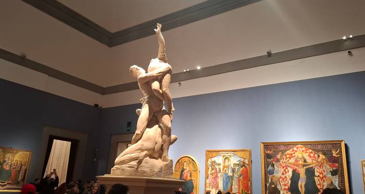 Standbeeld in een galerij met schilderijen aan de muren.