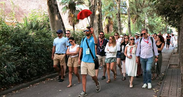 Groupe de touristes marchant sur un sentier avec des arbres et un guide tenant un drapeau rouge.