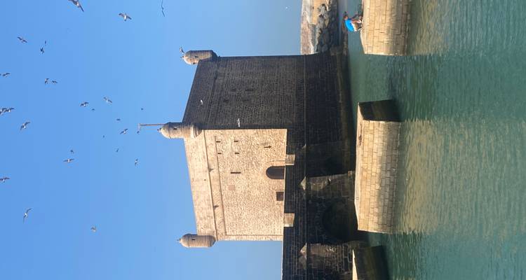 Historic stone fortress with a bridge, surrounded by water under a clear sky.