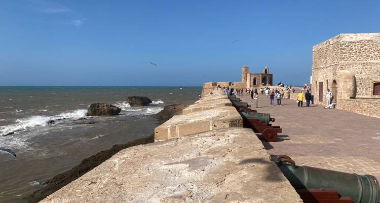 Historic coastal fortification with cannons, visitors walking along the path.